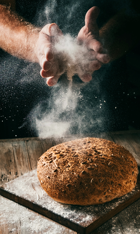 A baker putting flour on a fresh loaf of bread.
