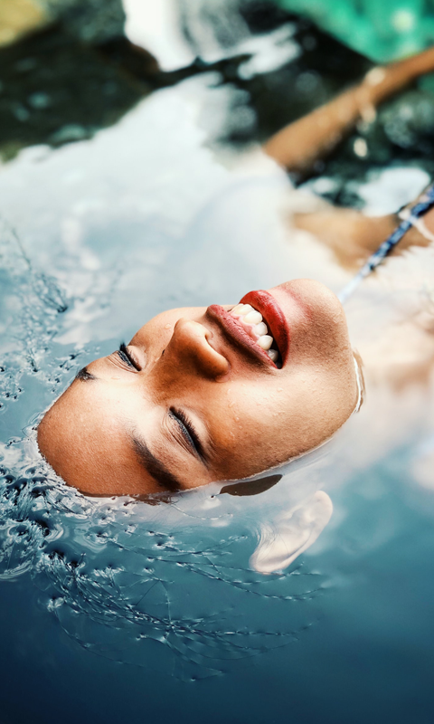 Woman smiling as her body is submerged under water and just her face is above the surface.